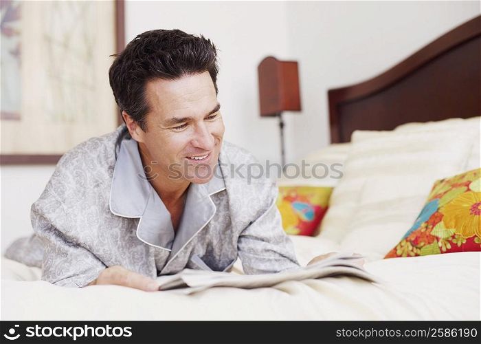 Mature man lying on the bed reading a newspaper