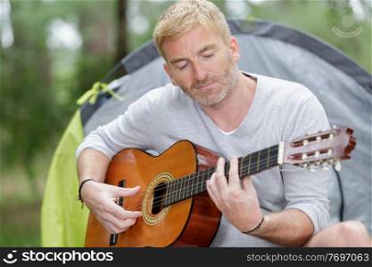 mature man near tent and playing guitar