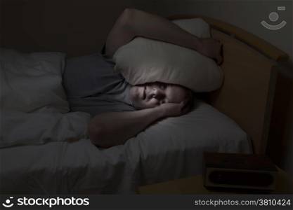 Mature man, pillow over head with eyes wide open, cannot sleep at night from insomnia