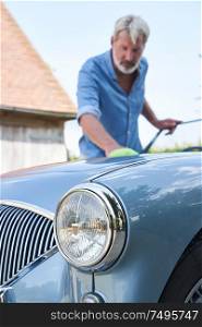 Mature Man Polishing Restored Classic Sports Car Outdoors At Home