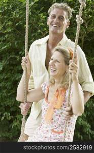 Mature man pushing a mature woman on a rope swing