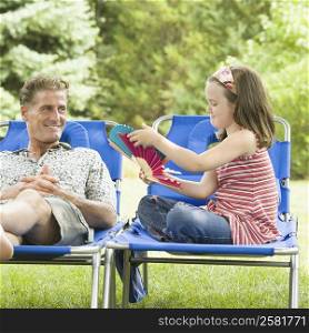 Mature man reclining on a lounge chair with his daughter sitting beside him