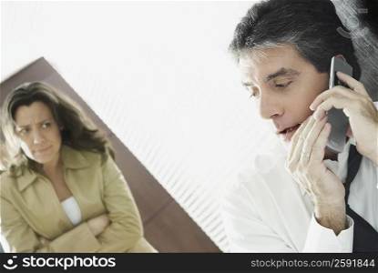 Mature man secretively talking on a mobile phone with his wife looking at him suspiciously