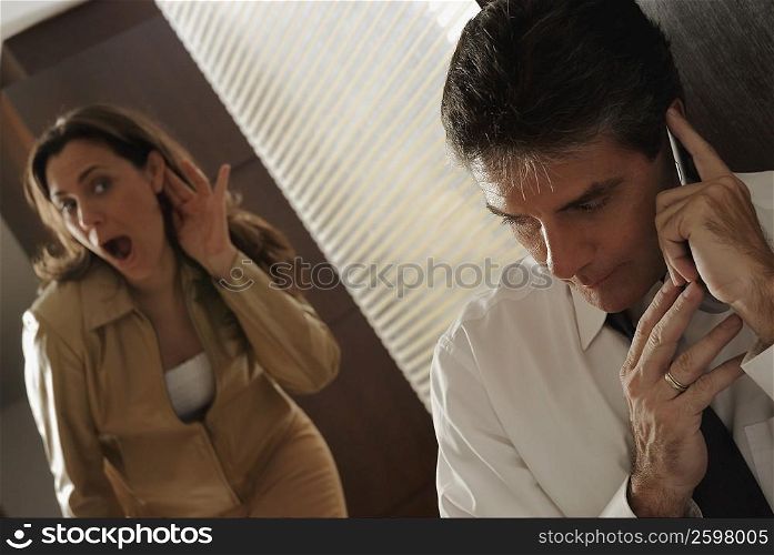 Mature man secretively talking on a mobile phone with his wife trying to listen in