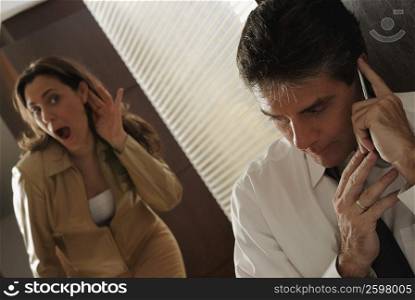 Mature man secretively talking on a mobile phone with his wife trying to listen in