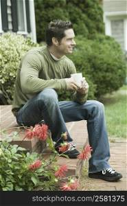 Mature man sitting at doorsteps and holding a cup of coffee