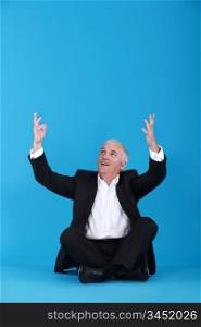 mature man sitting cross-legged with raised arms against blue background