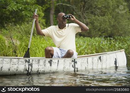 Mature man sitting in a canoe and looking through binoculars
