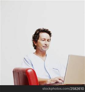 Mature man sitting in an armchair and using a laptop