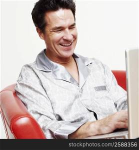 Mature man sitting in an armchair with a laptop and smiling