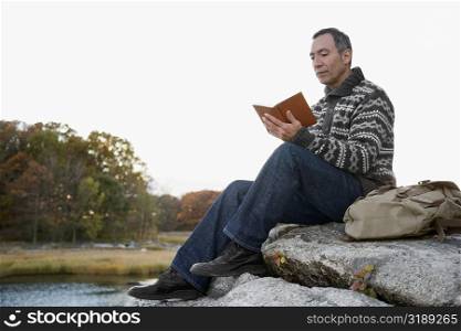 Mature man sitting on a rock and reading a book