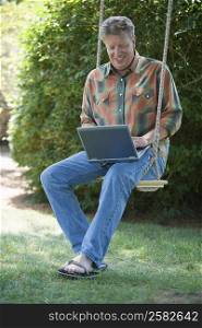 Mature man sitting on a swing and using a laptop