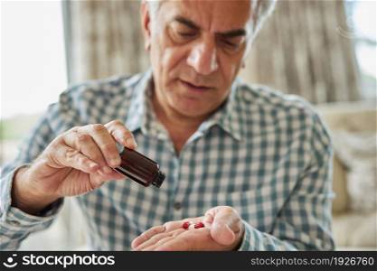 Mature Man Sitting On Sofa At Home Taking Medication Pills From Bottle