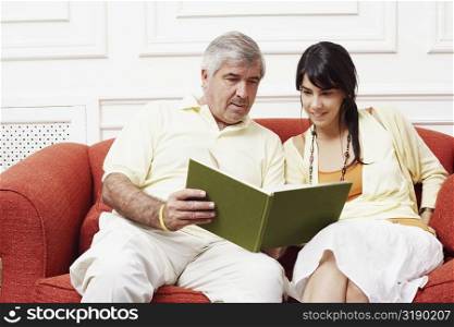Mature man sitting with his daughter on a couch and reading a book