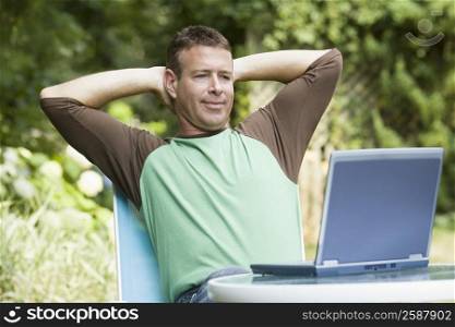 Mature man sitting with his hands behind head and looking at a laptop