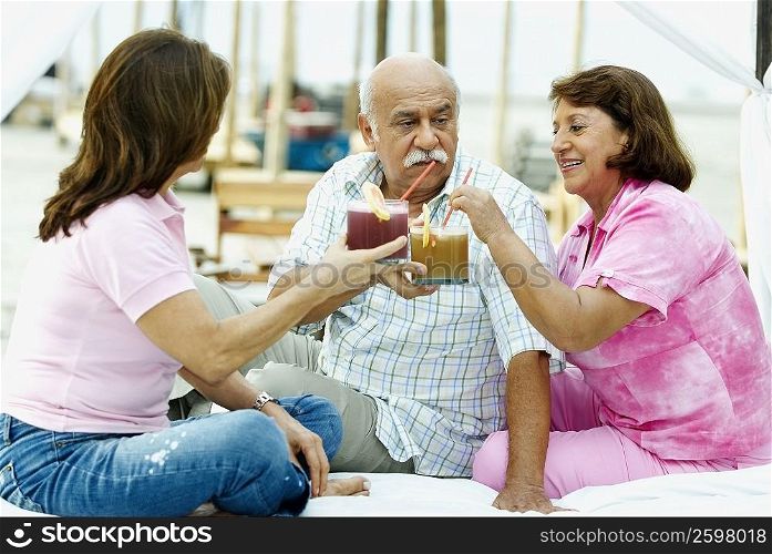 Mature man sitting with two mature women and holding glasses of juice