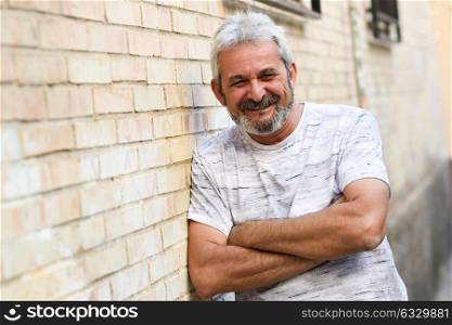 Mature man smiling at camera in urban background. Senior male with white hair and beard wearing casual clothes.