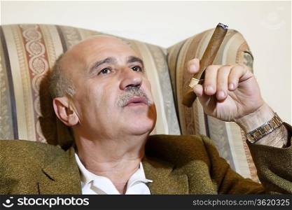 Mature man smoking cigar while relaxing on armchair