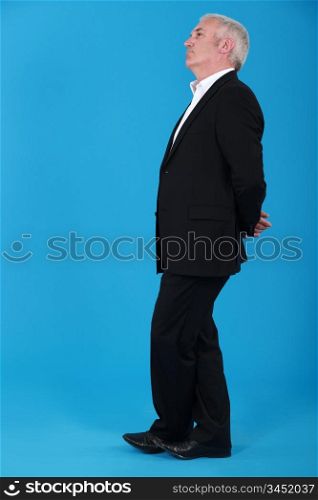 mature man standing in profile against blue background