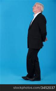 mature man standing in profile against blue background