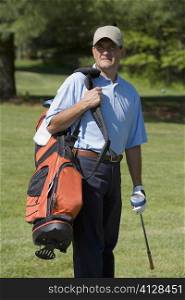 Mature man standing on a golf course carrying a golf bag with a golf club