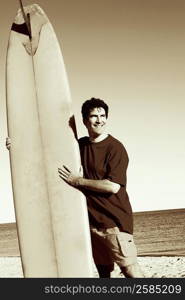 Mature man standing on the beach holding a surfboard