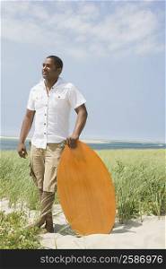 Mature man standing with a surfboard on the beach