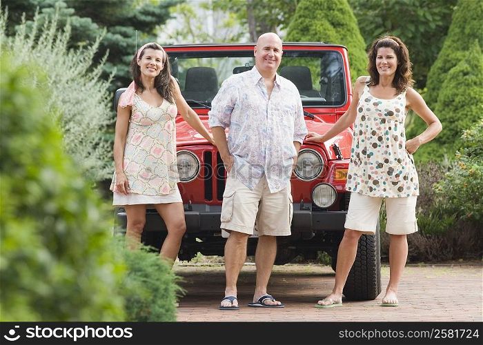 Mature man standing with two mature women in front of a jeep in a garden