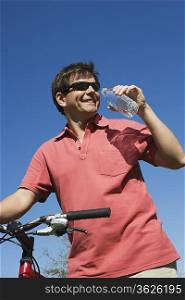 Mature man stands drinking water and holding bicycle handlebars