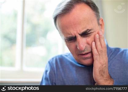 Mature Man Suffering With Toothache And Rubbing Painful Tooth