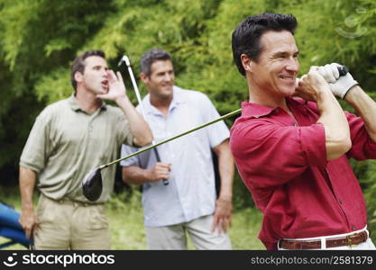 Mature man swinging a golf club with his friends standing behind him