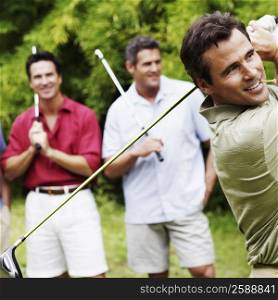 Mature man swinging a golf club with his friends standing behind him