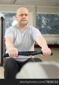 Mature man takes care of his health and he rowing in the gym