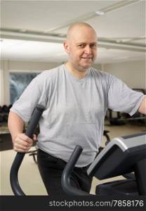 Mature man takes care of his health and he use elliptical trainer in the gym