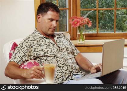 Mature man using a laptop and holding a mug of coffee