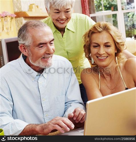 Mature man using a laptop with a mature woman and a senior woman smiling near him