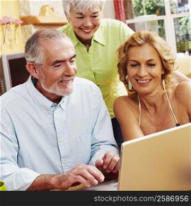 Mature man using a laptop with a mature woman and a senior woman smiling near him