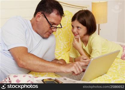Mature man using a laptop with his daughter lying beside him