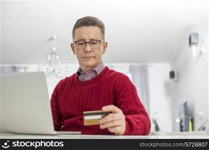 Mature man using credit card and laptop to shop online at home