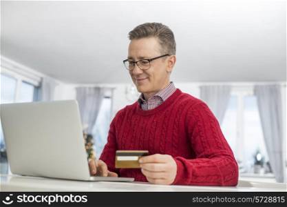 Mature man using credit card and laptop to shop online during Christmas