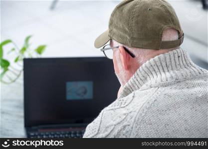 mature man with a baseball cap using a laptop, back view