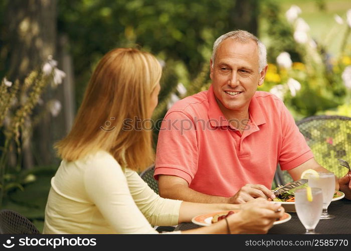 Mature man with a mid adult woman sitting at the table with plates of salad in front of them