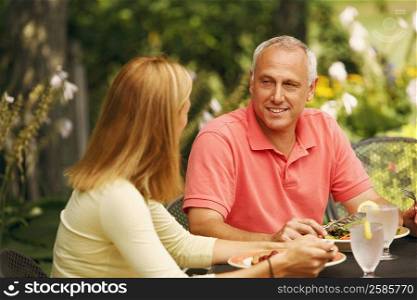 Mature man with a mid adult woman sitting at the table with plates of salad in front of them