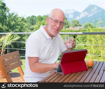 mature man with digital tablet on the terrace, drinking water