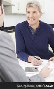 Mature Man With Financial Advisor Signing Document At Home