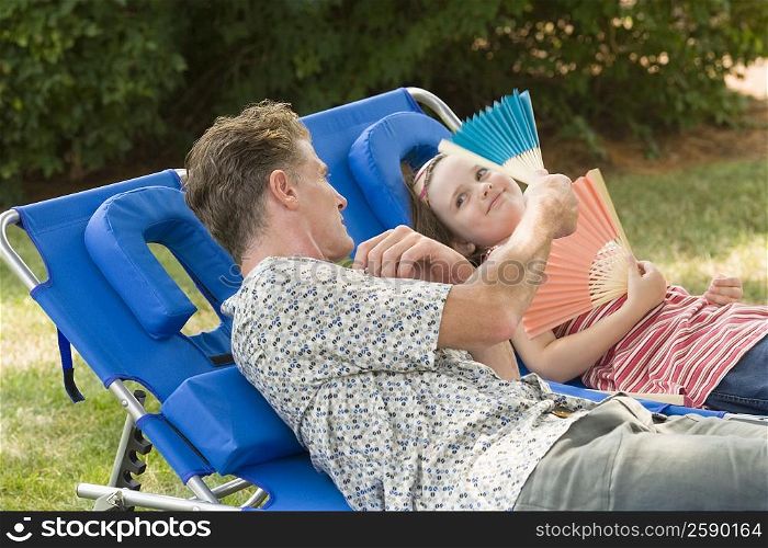 Mature man with his daughter reclining on lounge chairs in a lawn