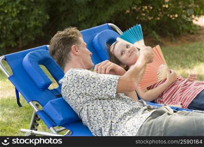 Mature man with his daughter reclining on lounge chairs in a lawn