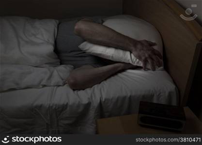 Mature man, with pillow covering entire face, cannot sleep at night from insomnia