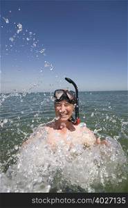 Mature man with snorkel splashing water