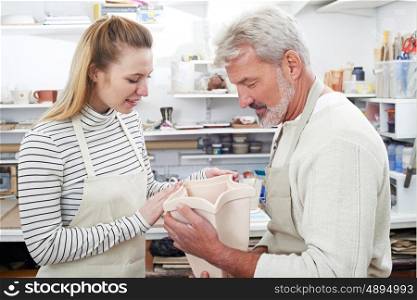 Mature Man With Teacher Looking At Vase In Pottery Class